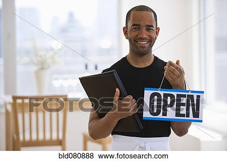 Stock Photo - Mixed race waiter in restaurant holding menu and open sign. Fotosearch