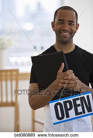 Stock Photo - Mixed race waiter in restaurant holding menu and open sign. Fotosearch