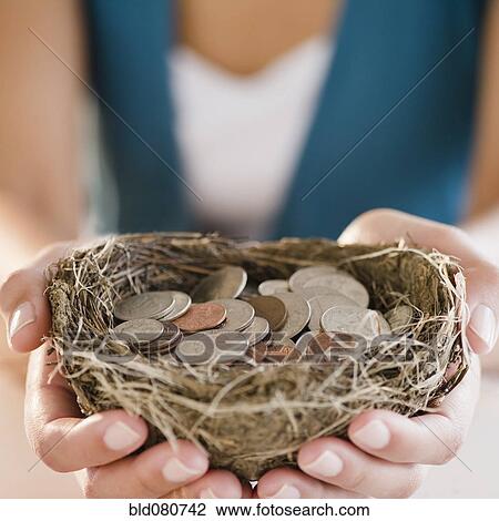 Stock Image - Mixed race woman holding nest filled with coins. Fotosearch