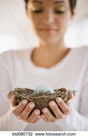 Stock Image - Mixed race woman holding nest with egg. Fotosearch