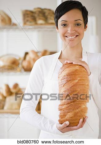 Stock Image - Mixed race woman in bakery holding bread. Fotosearch