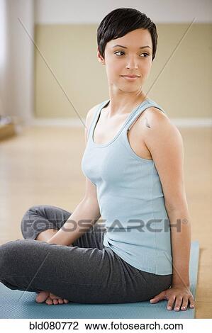 Stock Image - Mixed race woman sitting and stretching on exercise mat. Fotosearch