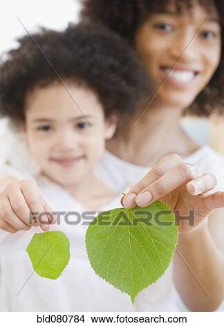 Picture - Mother and daughter holding green leaves. Fotosearch
