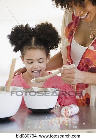 Picture - Mother feeding daughter from mixing bowl. Fotosearch