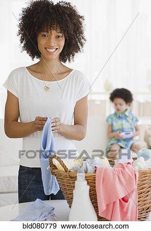 Mother folding laundry with daughter in background View Large Photo Image Stock Photo - Mother folding laundry with daughter in background. Fotosearch