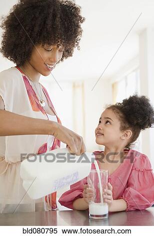 Stock Photography - Mother pouring milk into glass for daughter. Fotosearch
