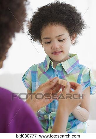 Stock Photo - Mother putting bandage on finger of daughter. Fotosearch