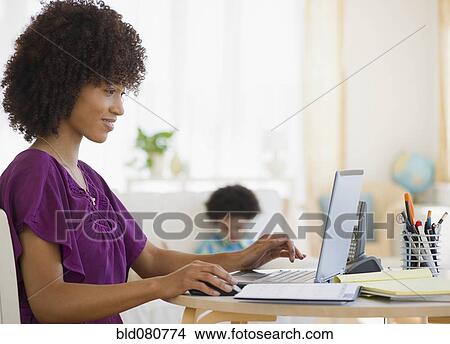 Picture - Mother working on laptop with child in background. Fotosearch