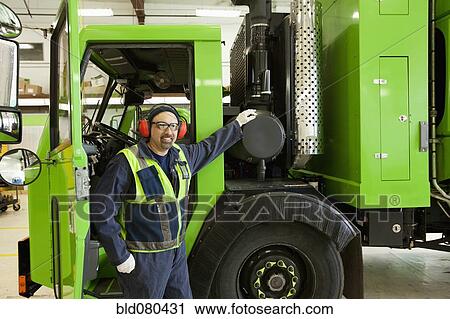 Stock Image - Pacific Islander man standing by garbage truck. Fotosearch