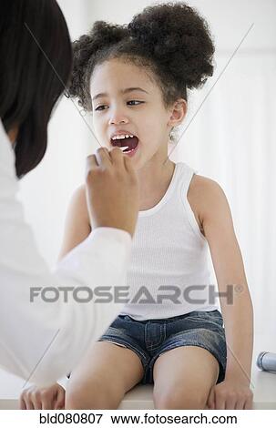 Stock Photo - Pediatrician with tongue depressor examining patient. Fotosearch