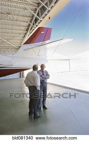 Stock Image - Hispanic businessmen standing in airplane hangar. Fotosearch