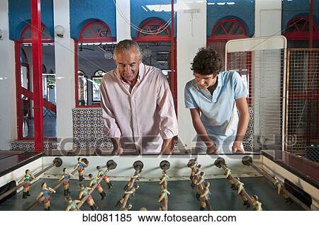 Stock Photography - Hispanic grandfather and grandson playing foosball. Fotosearch