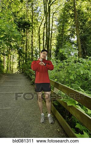 Stock Image - Mixed race man checking pulse after exercise in forest. Fotosearch