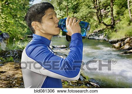 Stock Photograph - Mixed race man drinking water near river. Fotosearch