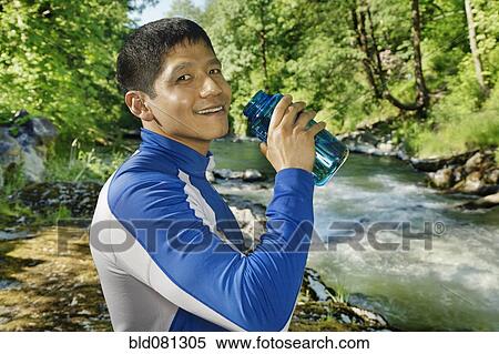 Stock Photography - Mixed race man drinking water near river. Fotosearch
