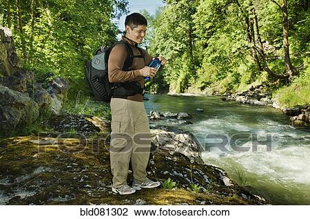 Stock Image - Mixed race man hiking near river. Fotosearch