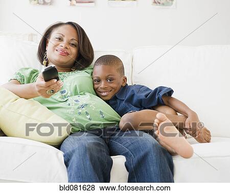 Stock Photo - Black mother and son watching TV on living room sofa. Fotosearch