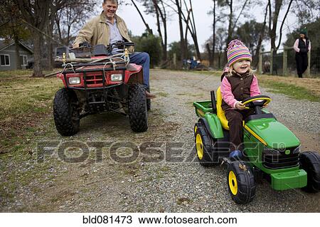 Stock Image - Caucasian grandfather and granddaughter on tractors. Fotosearch
