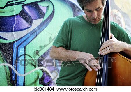 Picture - Caucasian man playing double bass in front of graffiti covered wall. Fotosearch