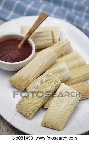Stock Image - Close up of corn tamales and red sauce on plate. Fotosearch