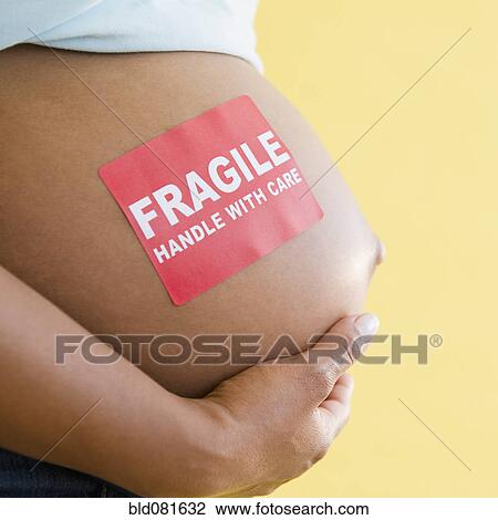 Stock Image - Close up of 'Fragile' sticker on pregnant Black woman's stomach. Fotosearch