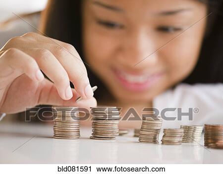 Stock Image - Close up of mixed race teenage girl stacking coins. Fotosearch