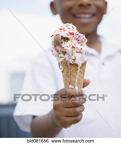 Stock Photograph - Close up of smiling Black boy holding melting ice cream cone. Fotosearch