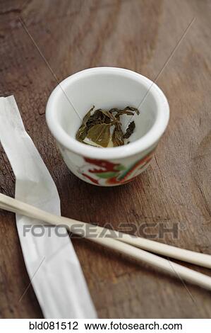 Stock Image - Close up of tea leaves in cup next to chopsticks. Fotosearch
