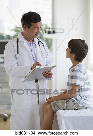 Picture - Doctor with medical chart talking to boy in examination room. Fotosearch