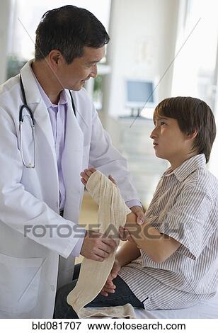 Stock Photo - Doctor wrapping boy's hand with bandage in examination room. Fotosearch