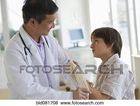 Stock Photo - Doctor wrapping boy's hand with bandage in examination room. Fotosearch