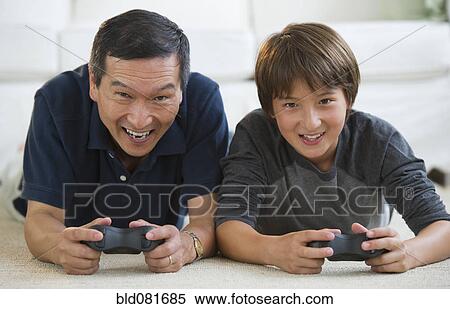 Stock Photography - Father and son playing video game on living room floor. Fotosearch