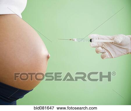 Stock Photo - Gloved hand pointing needle at pregnant woman's stomach. Fotosearch
