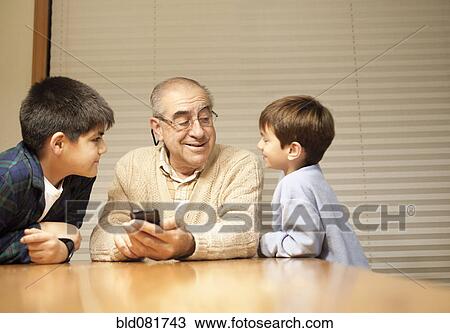 Stock Image - Grandfather and grandsons with cell phone at table. Fotosearch