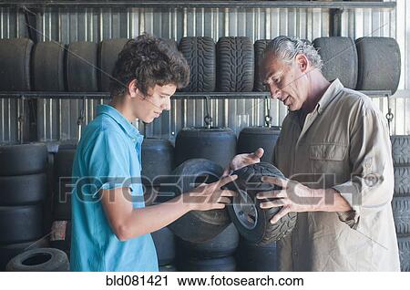 Stock Image - Hispanic grandfather and grandson looking at go-cart tires. Fotosearch