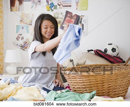 Picture - Mixed race teenage girl doing laundry on bed. Fotosearch