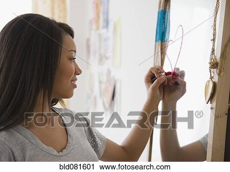 Stock Image - Mixed race teenage girl drawing heart on mirror with lipstick. Fotosearch