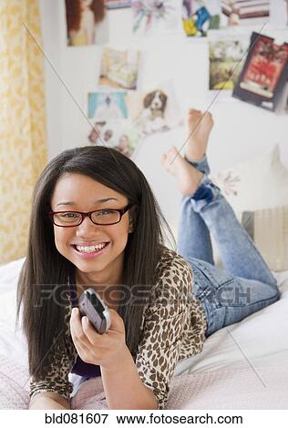 Mixed race teenage girl holding remote control and laying on bed View Large Photo Image Stock Photo - Mixed race teenage girl holding remote control and laying on bed. Fotosearch
