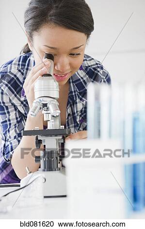 Stock Image - Mixed race teenage girl looking through microscope. Fotosearch