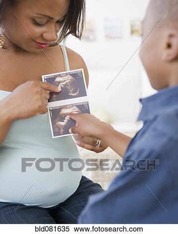 Stock Photography - Pregnant Black mother showing sonogram to son. Fotosearch