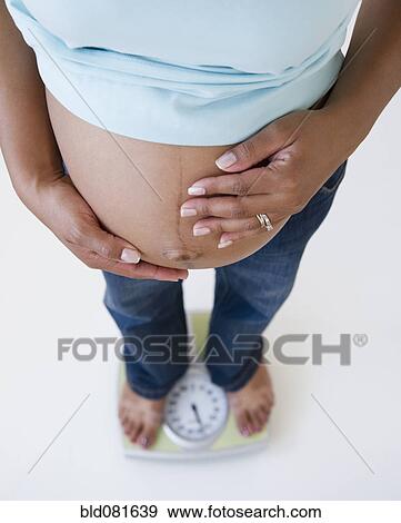 Pregnant Black woman holding stomach and standing on scale View Large Photo Image Stock Photo - Pregnant Black woman holding stomach and standing on scale. Fotosearch