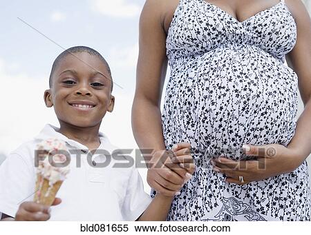 Stock Photography - Smiling Black boy holding melting ice cream cone and pregnant mother's hand. Fotosearch