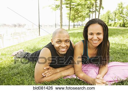 Stock Photograph - Smiling couple laying in grass at park. Fotosearch