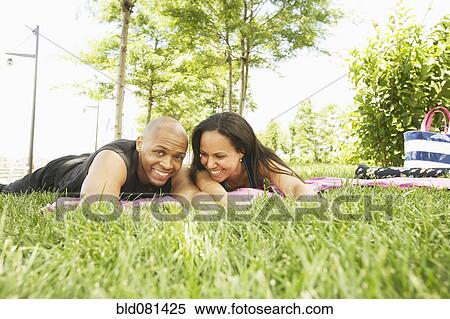 Stock Photography - Smiling couple laying in grass at park. Fotosearch