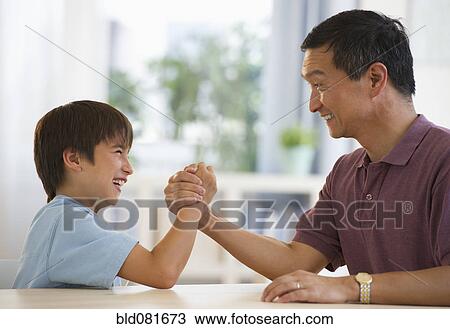 Smiling father and son arm wrestling at table View Large Photo Image Stock Image - Smiling father and son arm wrestling at table. Fotosearch