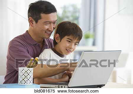 Stock Photography - Smiling father and son using laptop. Fotosearch