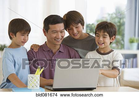 Picture - Smiling father and sons using laptop. Fotosearch
