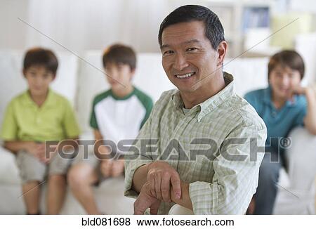 Stock Photo - Smiling father in living room with sons in background. Fotosearch