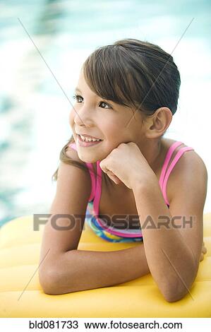Stock Image - Smiling mixed race girl leaning on pool raft. Fotosearch