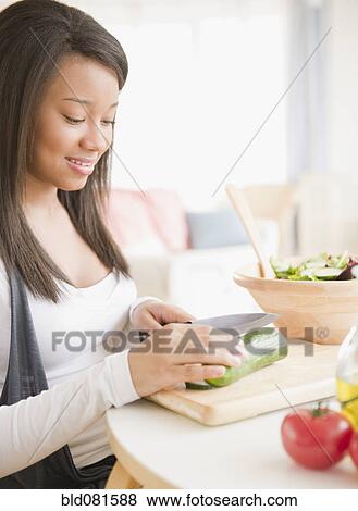 Stock Photo - Smiling mixed race teenage girl cutting vegetables. Fotosearch